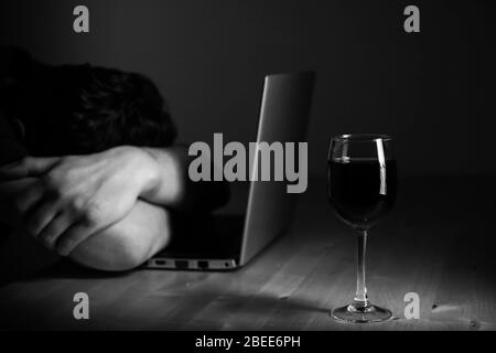 Home office and alcoholism problem - depressed man sitting in front of computer, he hide his face. Wine glass on the table Stock Photo