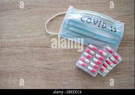 Medical face mask with text covid-19 and Antibiotics on wooden table. Concept Coronavirus, Covid-19 Stock Photo