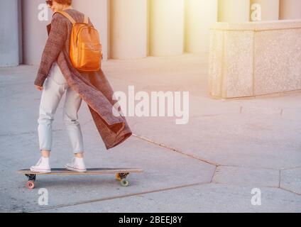 Young happy short-haired brunette woman is riding skateboard in a city. Stock Photo