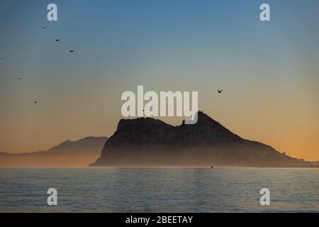 Birds flying around the of Gibraltar seen at sunset from Alcaidesa beach in Spain Stock Photo