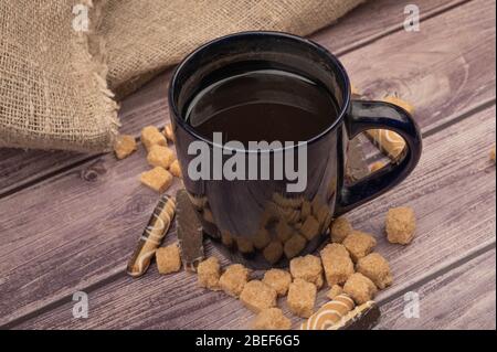 Dark blue ceramic mug with tea and pieces of brown cane sugar on a wooden background. Close up Stock Photo
