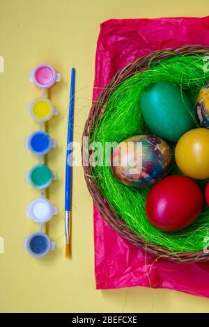 Green grass nest in a basket with colored chicken Easter eggs, multicolored painted eggs and paints, Easter tradition, celebration concept Stock Photo