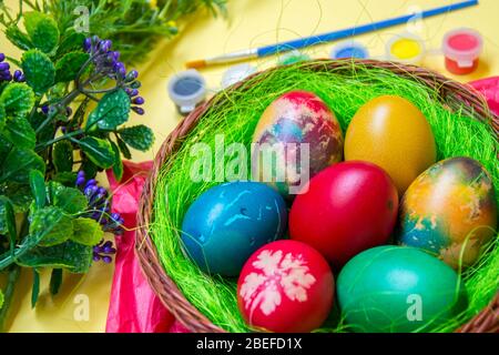 Green grass nest in a basket with colored chicken Easter eggs, multicolored painted eggs,paints and plastic flowers, Easter tradition, celebration Stock Photo