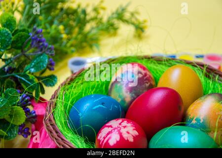 Green grass nest in a basket with colored chicken Easter eggs, multicolored painted eggs,paints and plastic flowers, Easter tradition, celebration Stock Photo