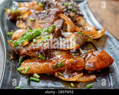 Roasted chilli pork served in a black plate over moody background. Selective focus Stock Photo