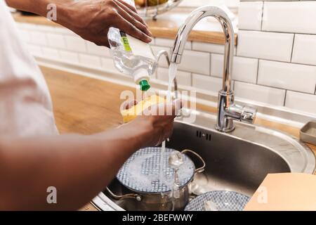 Cropped picture of young african guy in the morning at the kitchen wash the dishes. Stock Photo