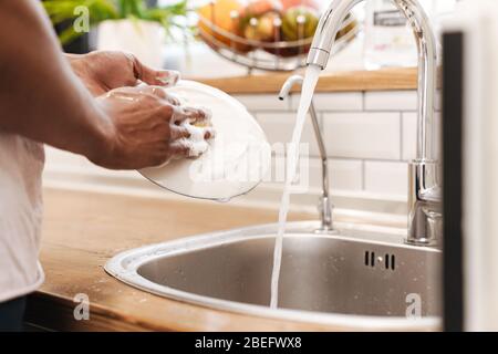 Cropped picture of young african guy in the morning at the kitchen wash the dishes. Stock Photo