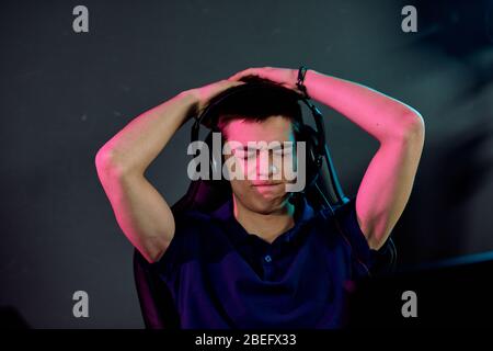 Frustrated young man in headset holding head in hands while he has lost in network game Stock Photo