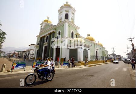 Guacara, Carabobo, Venezuela. 13th Apr, 2020. April 13, 2020. A couple travels by them motorcycle, in front of the principal church of the town.Located in the Marques del toro street of the central town of Guacara, Carabobo state. Photo: Juan Carlos Hernandez Credit: Juan Carlos Hernandez/ZUMA Wire/Alamy Live News Stock Photo