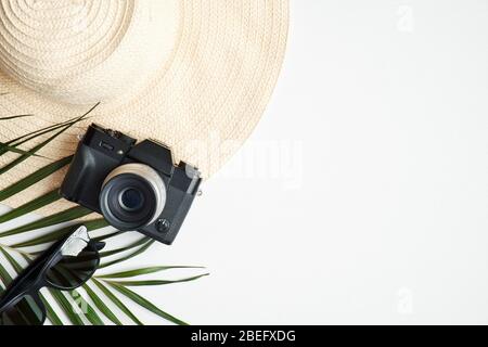 Flat lay female fashion outfit on white table. Top view beach straw hat, vintage camera, sunglasses and tropical palm leaf. Travel, holiday, vacation Stock Photo