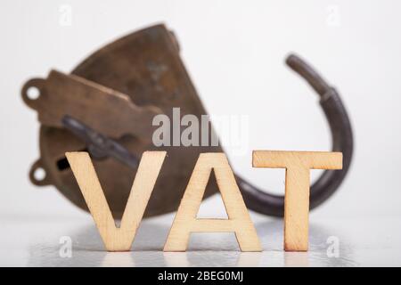 The inscription VAT made of wooden letters. Taxes and an old padlock. Light background. Stock Photo