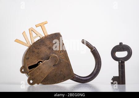 The inscription VAT made of wooden letters. Old antique padlock and key. Light background. Stock Photo
