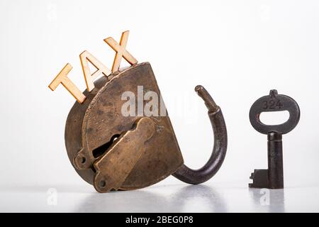 TAX inscription made of wooden letters. Old antique padlock and key. Light background. Stock Photo