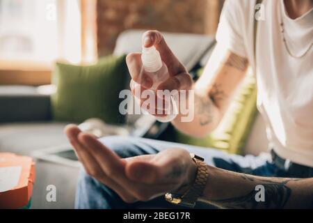 Disinfecting. Man studying at home during online courses, smart school. Getting classes or profession while isolated, quarantine against coronavirus spreading. Using laptop, smartphone, headphones. Stock Photo