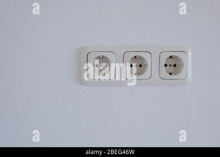 Real triple European socket or outlet Type F on white painted plaster interior wall. Stock Photo