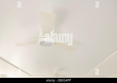 An overhead LED luminaire combined with a white ceiling fan on a white ceiling. Stock Photo