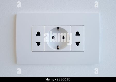 A block of white outlets consisting of one EU standard outlet with grounding and two US standard sockets. Stock Photo