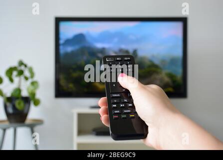 Watching TV. A woman's hand holding the TV remote control with a television in the background. Nature, documentary, tv screen, binge watching Stock Photo