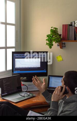 Young man working at home while talking on the phone. Programmer working from home. Concept of teleworking or telecommuting. Stock Photo