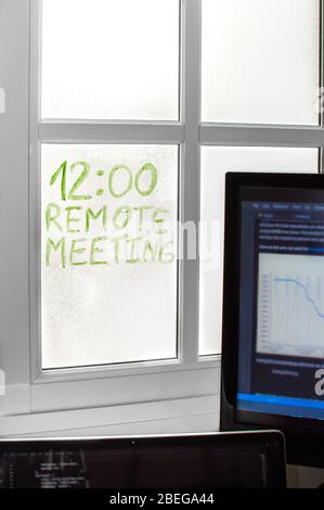 Space with devices at home to teleworking, detail of a reminder written on the window 'Remote Meeting'. Concept of working from home, telecommuting. Stock Photo