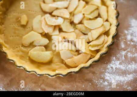 woman adds sliced apples to apple pie. Woman hands working a pie dough in a tray, on a kitchen table, surrounded by pumpkin pie ingredients. Tradition Stock Photo