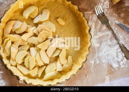 woman adds sliced apples to apple pie. Woman hands working a pie dough in a tray, on a kitchen table, surrounded by pumpkin pie ingredients. Tradition Stock Photo