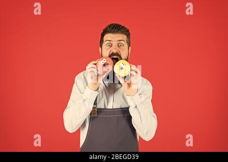 Carbs and calories. Bakery owner. Bakery business. Baked goods. Sweets and cakes. Junk food. Hipster bearded baker eat donuts. Doughnut bakery. Bearded cheerful well groomed man selling donuts. Stock Photo