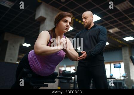 Trainer helps to overweight woman, gym Stock Photo