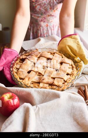 the housewife in the kitchen mittens delivers the apple pie to the table. Homemade apple tart. Woman putting delicious american pie on table Stock Photo