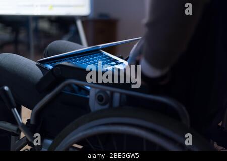 Disabled businessman in the wheelchair works in the office at the computer while performing in co-working space. Disability and handicap concept. Hori Stock Photo
