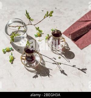 Spring sunny morning, cups with fruit tea, napkin and young tender tree branches, openwork shadows on the table Stock Photo