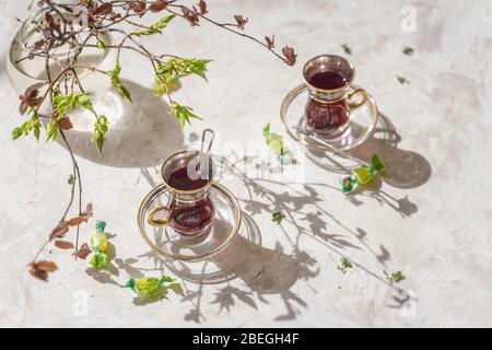 Young tender branches of colorful color, shadows on the table, cups with fruit tea, openwork background. Spring sunny morning Stock Photo