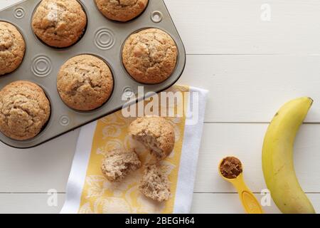 Banana Nut Muffins, Banana, Cinnamon and Kitchen Towel on White Wood Background with Copy Space Stock Photo