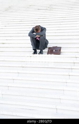 Unrecognizable businessman sitting outdoors on a large set of white steps with his head in his hands Stock Photo