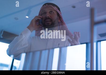 Middle Eastern businessman talking on the phone and looking out the window in his office. Businessman Arabic using mobile phone for connection to comm Stock Photo