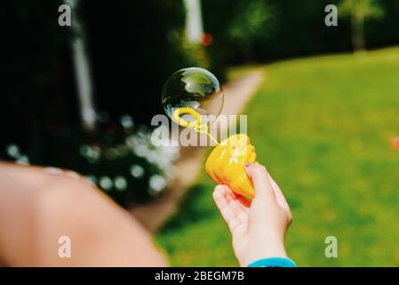 Child's hand holding a soap bubble while playing in summer. Stock Photo