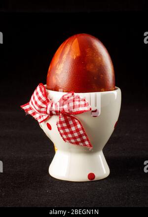 Traditionally brown painted Easter egg in the egg cup isolated on the black background Stock Photo