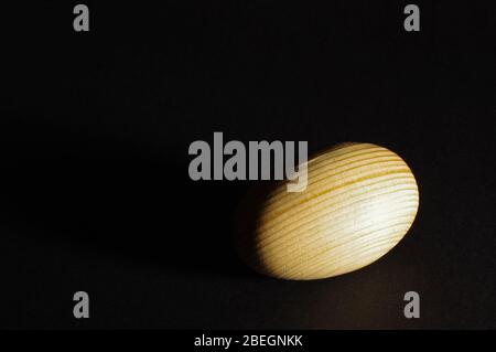 Wooden artificial egg under hard light on the black background Stock Photo