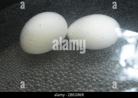 A closeup view of two white eggs in the boiling water and bubbles in the background.An Easter day special cooking photography with Nikon camera on apr Stock Photo