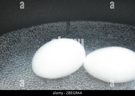 A closeup view of two white eggs in the boiling water and bubbles in the background.An Easter day special cooking photography with Nikon camera on apr Stock Photo