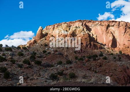 A colorful desert mesa with sandstone rock formations and high cliffs illuminated by the sun through a break in the clouds in northern New Mexico Stock Photo