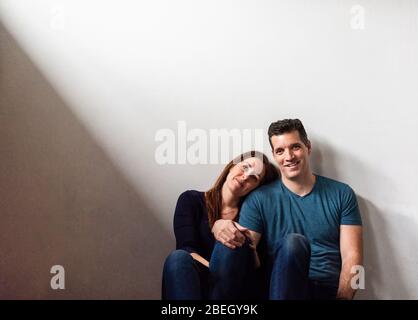 Cropped image of a couple sitting together against a white wall. Stock Photo