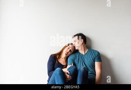 Cropped image of loving couple sitting together against a white wall. Stock Photo