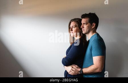 Couple standing close together in a patch of light against white wall. Stock Photo