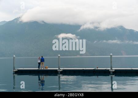 Man and woman standing on dock looking at foggy mountans Stock Photo