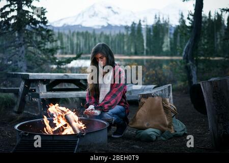 Young Woman crouching by fire warming hands Stock Photo