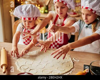 Three little chefs enjoying in the kitchen making cakes. Girls at the kitchen. Family housekeeping. Stock Photo