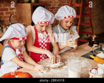 Three little chefs enjoying in the kitchen making cakes. Girls at the kitchen. Family housekeeping Stock Photo