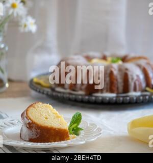 Lemon Ricotta Bundt Cake with icing displayed on a black decorative plate with Daisy flowers in a vase in the background. Stock Photo