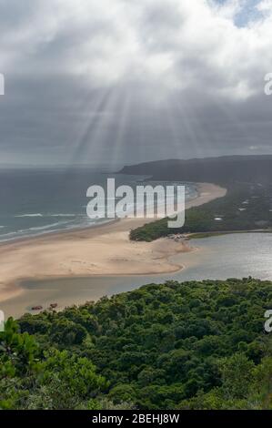 Aerial landscape of beautiful sandy beach with sun shining through clouds and green summer forest on the foreground. Natures Valley, Garden Route Sout Stock Photo